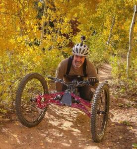 A smiling man barrels down an autumn trail on his adapted mountain bike. 
