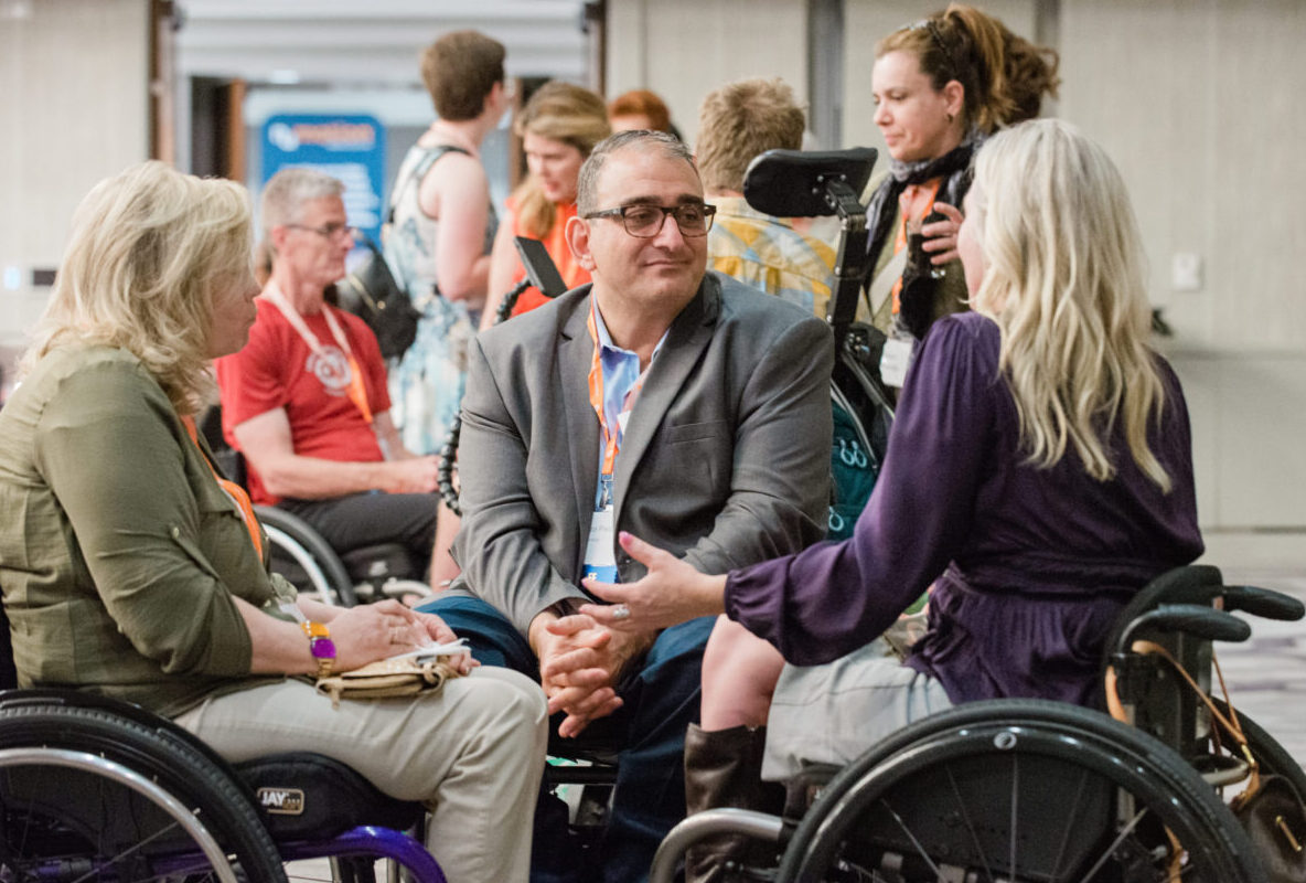 A man wearing glasses and using a wheelchair listens to a woman wheelchair user.