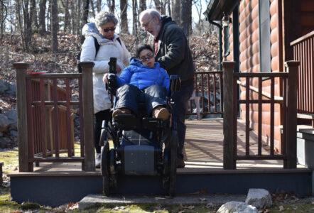 A Latina with curly black hair and eyeglasses gingerly descends a few porch steps while using an iBOT.
