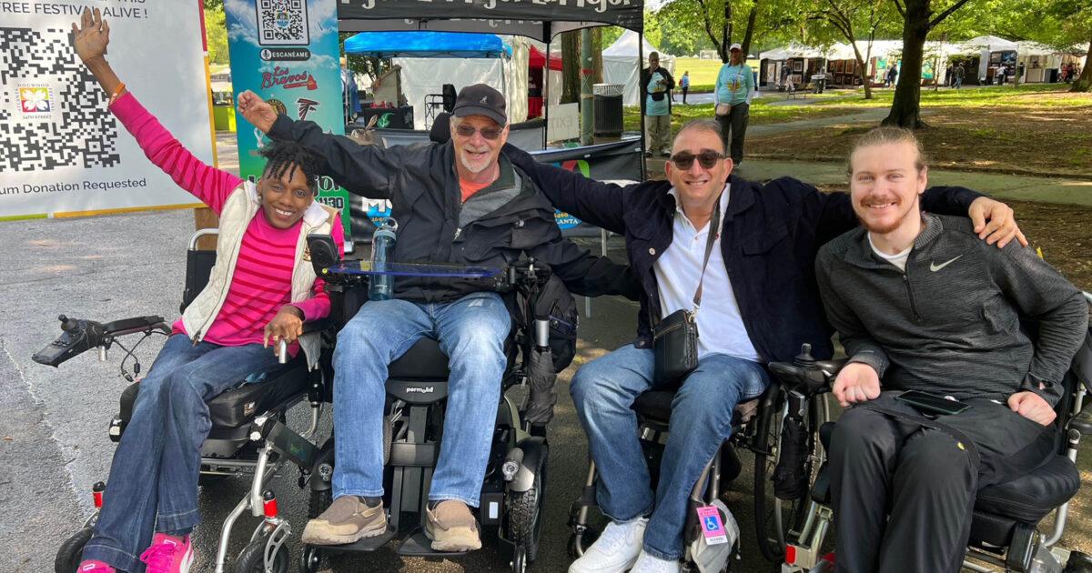 Four wheelchair users cheer and smile. They are of different races and genders.