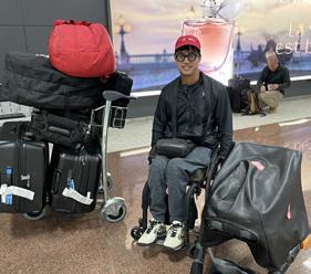 man in wheelchair in airport next to cart stacked with suitcases