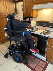 A man in a power wheelchair uses his seat elevation to cook independently.