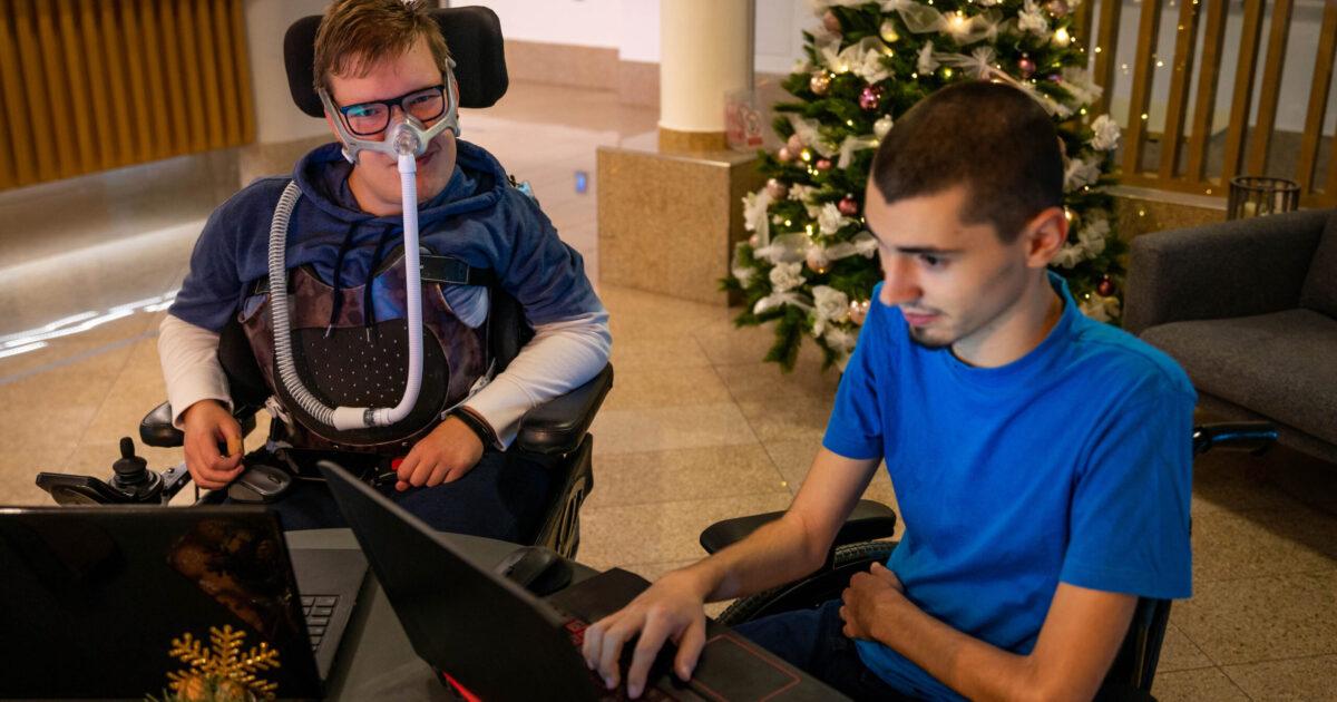 Two young men, both wheelchairs and one a vent user, use their laptops.