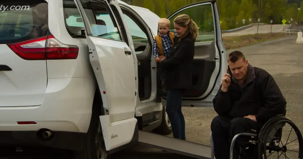 woman holding baby, man in wheelchair about to enter accessible van
