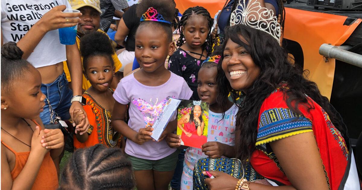 A beautiful Black woman in a tiara speaks with young Black girls.