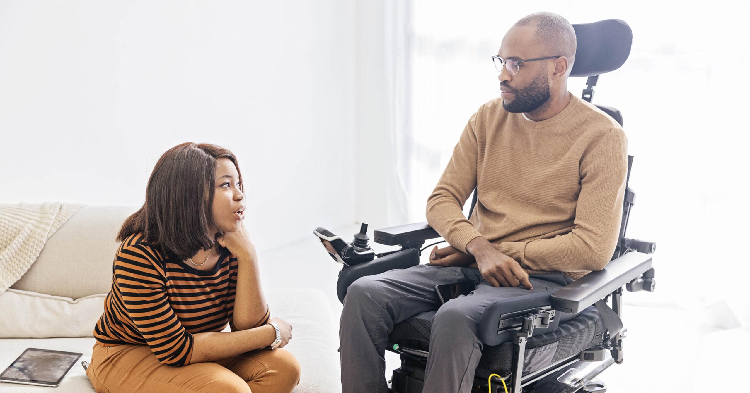 A Black powerchair user talks with a Black woman