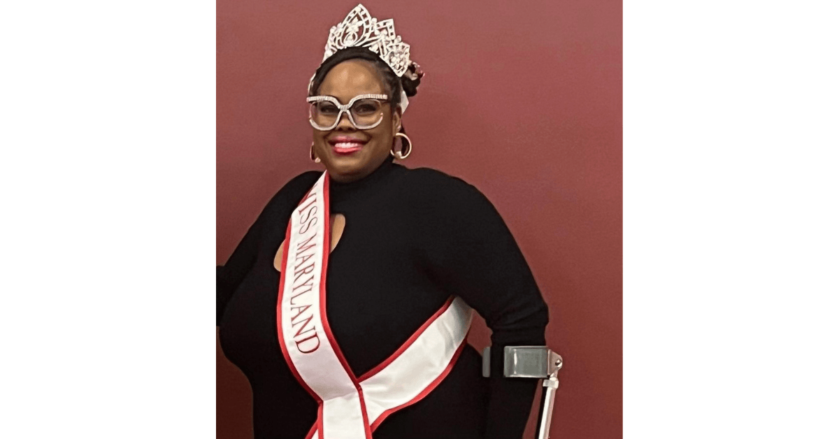 Monica Wiley, a black woman, stands with crutches wearing her pageant sash and crown.