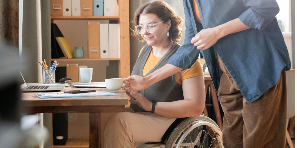 Woman in casualwear servving a cup of tea to young woman in wheelchair