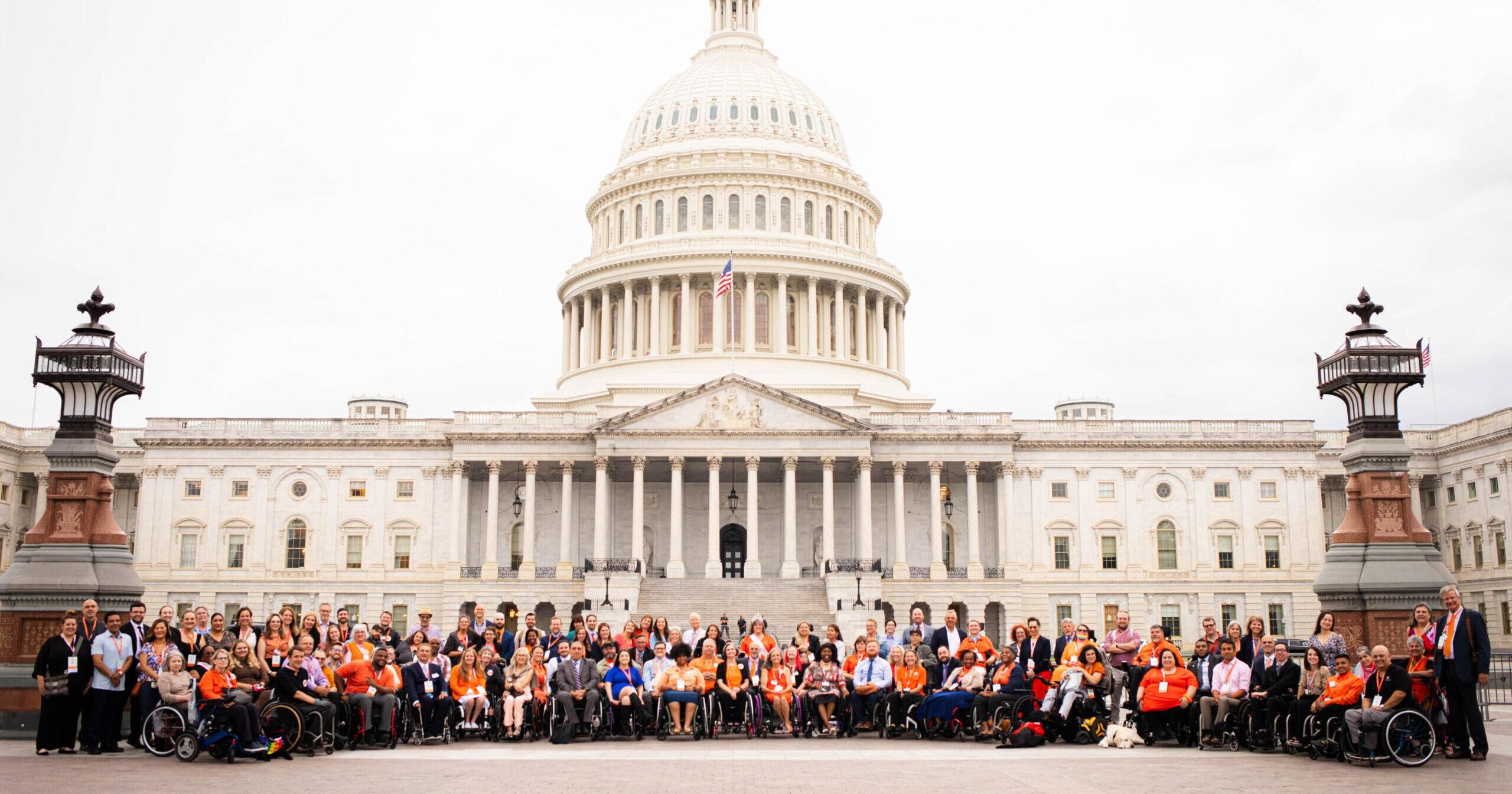A diverse group of United Spinal advocates in wheelchairs and their allies smile in from of Capitol Hill.