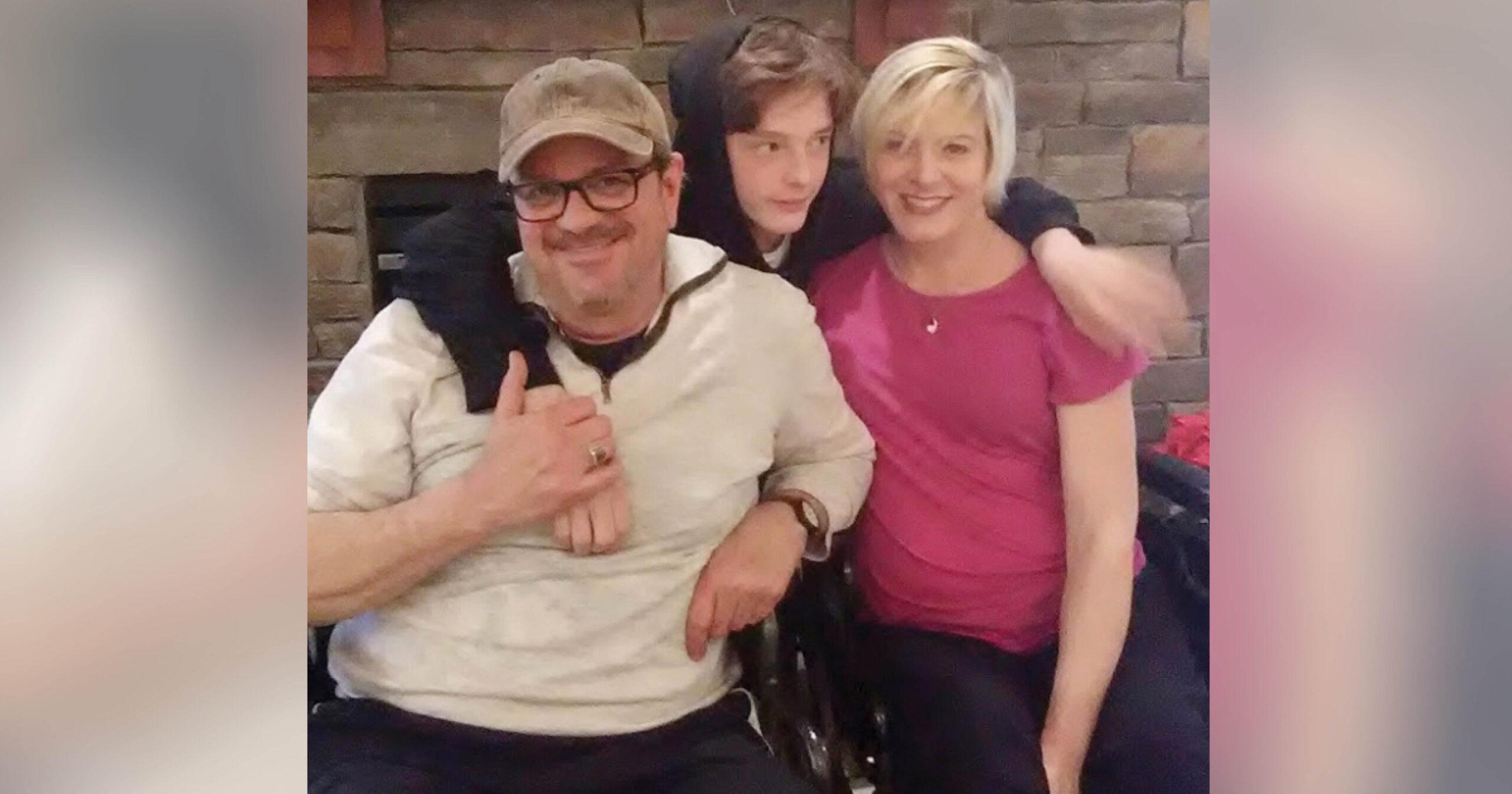 This is a family photo of man, a teenaged boy and a woman with a spinal cord injury. The boy has his arms draped around the shoulders of his parents.
