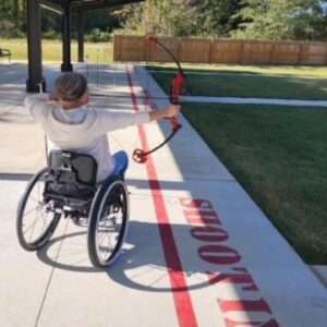 Erin Gildner, a white woman in a manual wheelchair doing archery