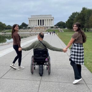 man in wheelchair in Washington DC park holding hands with young women on either side