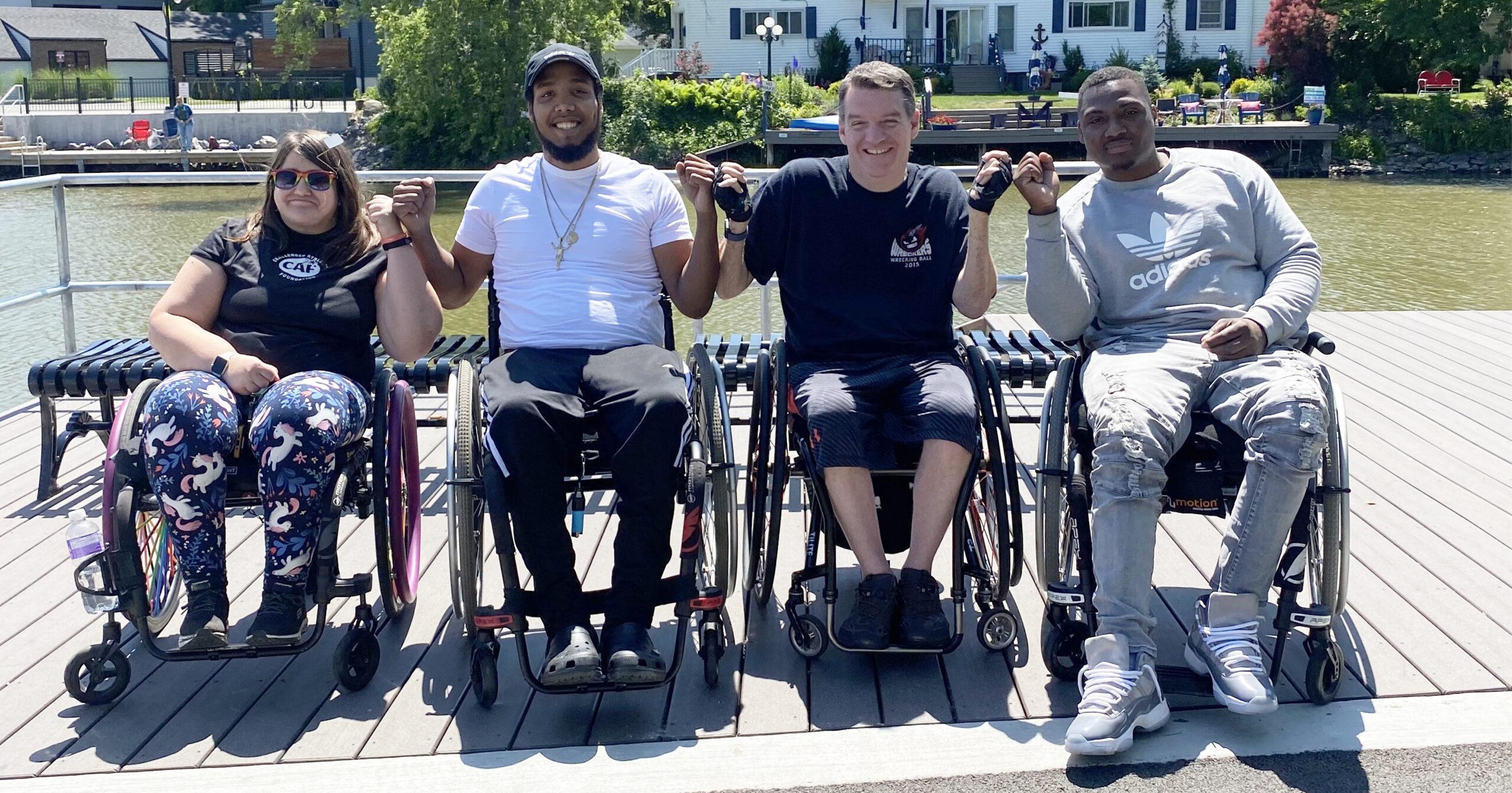 four wheelchair users on a pier giving the person next to them a fist bump