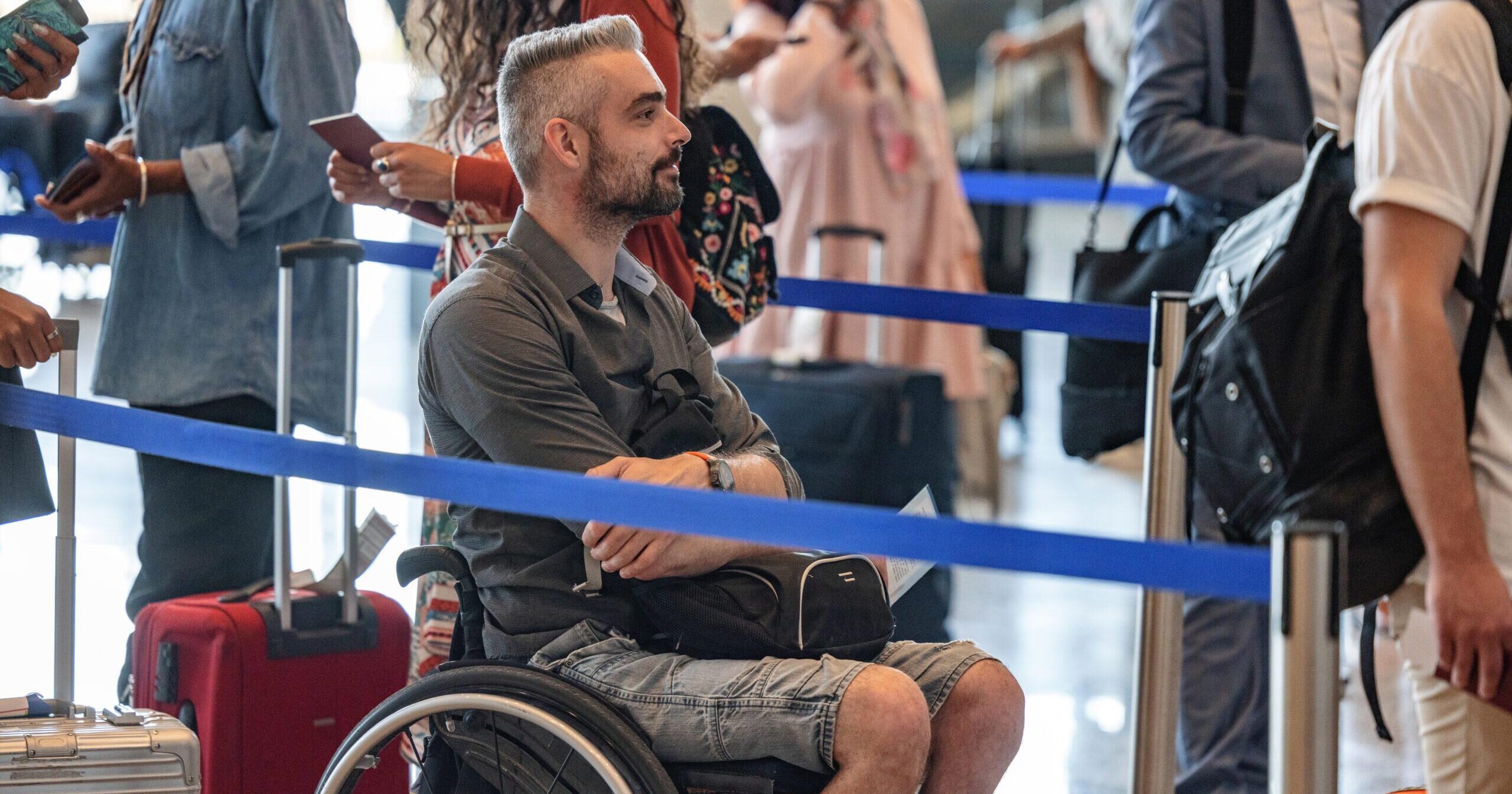 A Caucasian man in a wheelchair waiting in a queue at the airport.