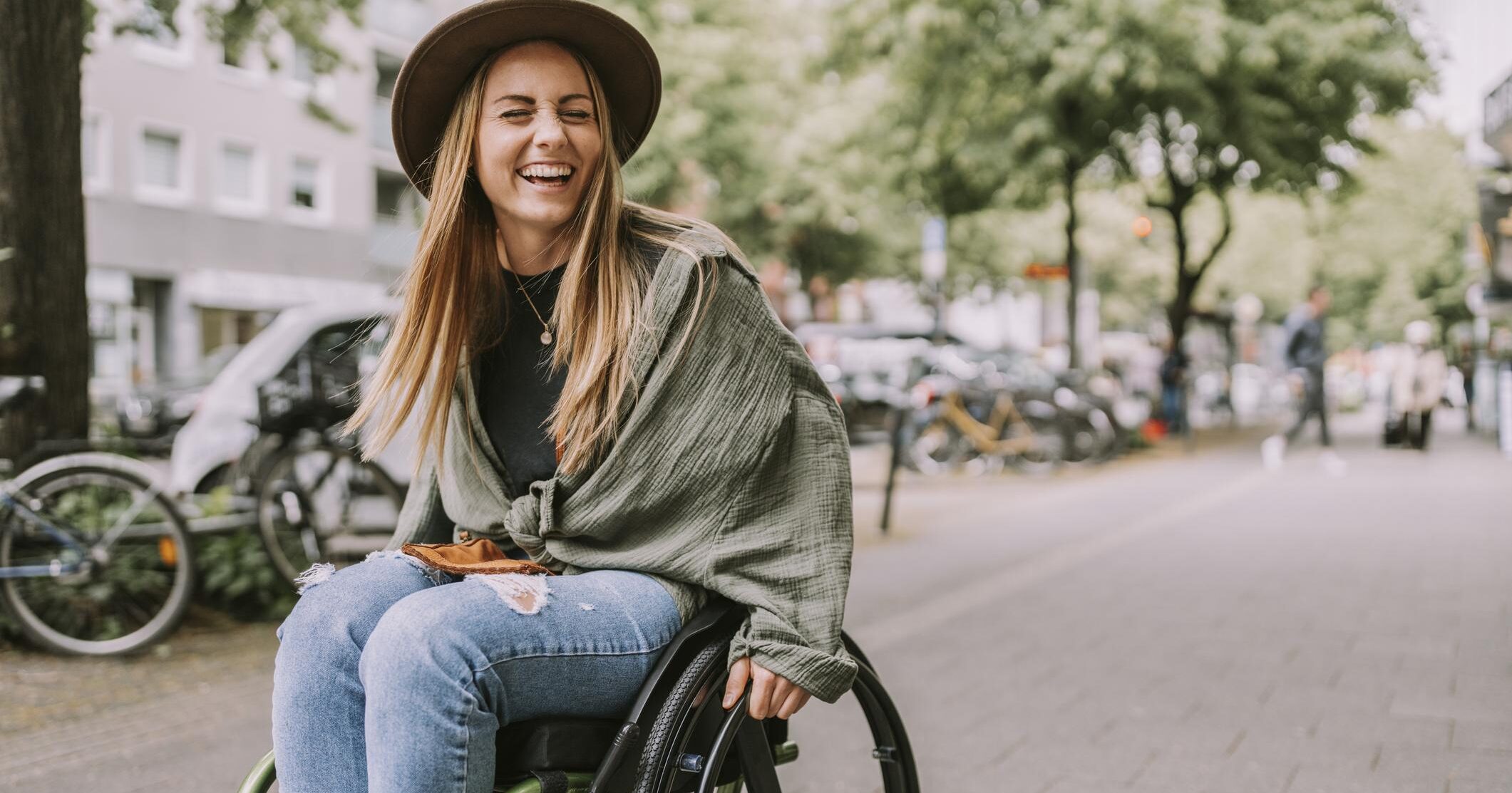 Cheerful young woman sitting on wheelchair at sidewalk