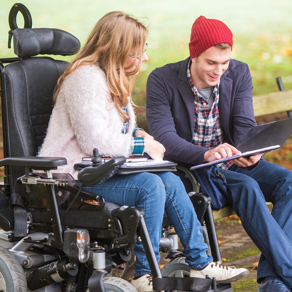 woman in powerchair talking to man on a bench