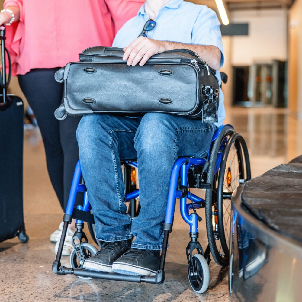 Close-up of a handicap Caucasian man sitting in his wheelchair next to his blonde mature girlfriend who is always attentive to his needs at the airport.
