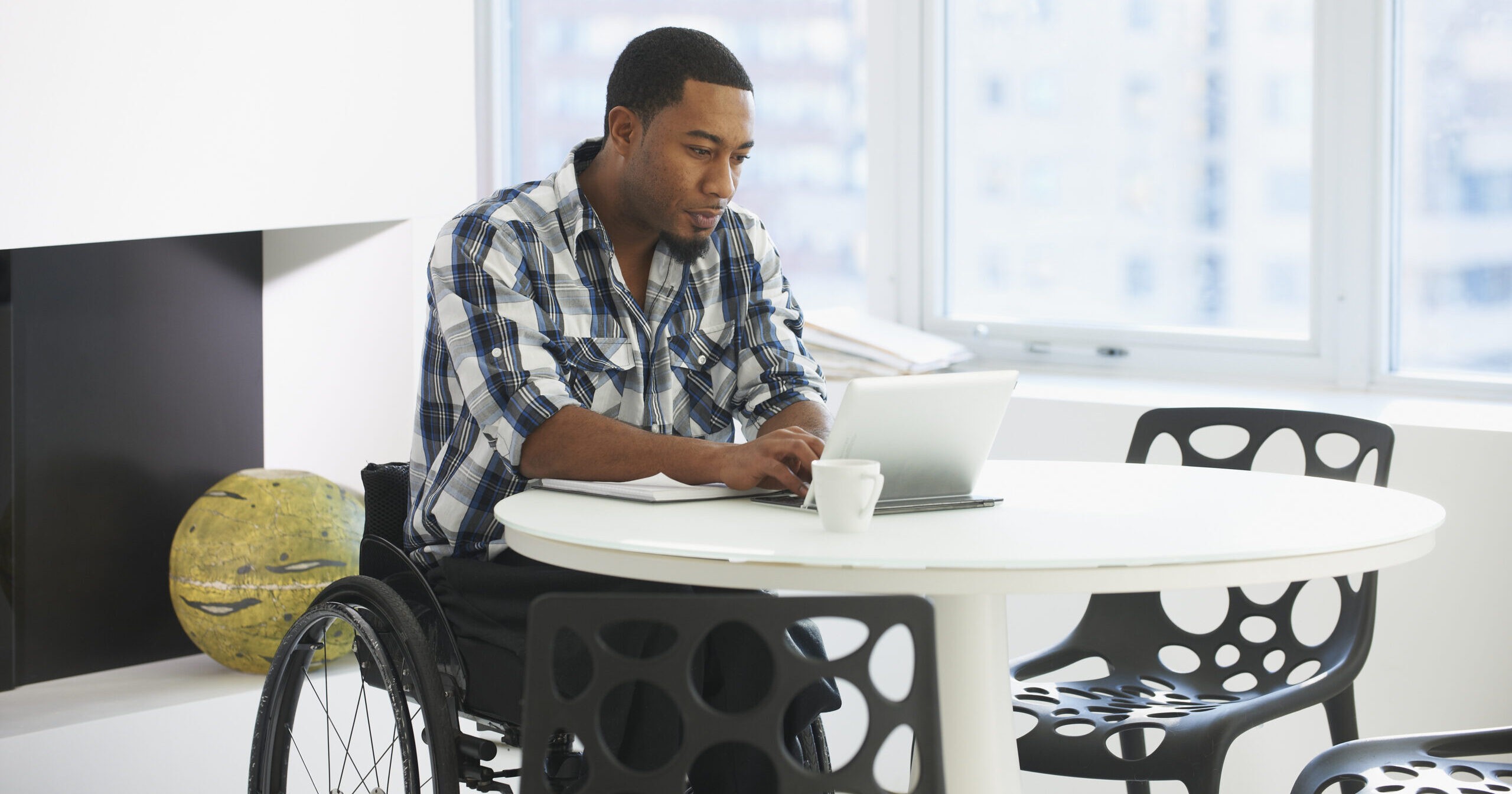 Black businessman in wheelchair using laptop at table