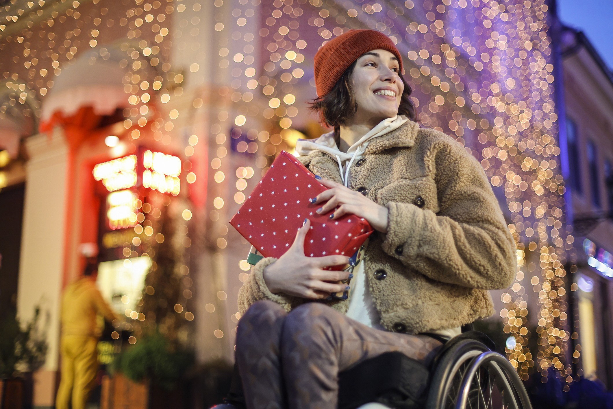Young disabled woman in a wheelchair celebrating holidays in a city street. About 30 years old, Caucasian brunette.