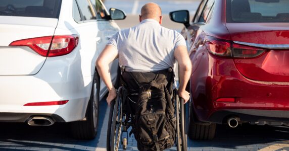 Person with a physical disability getting in red car from wheelchair.
