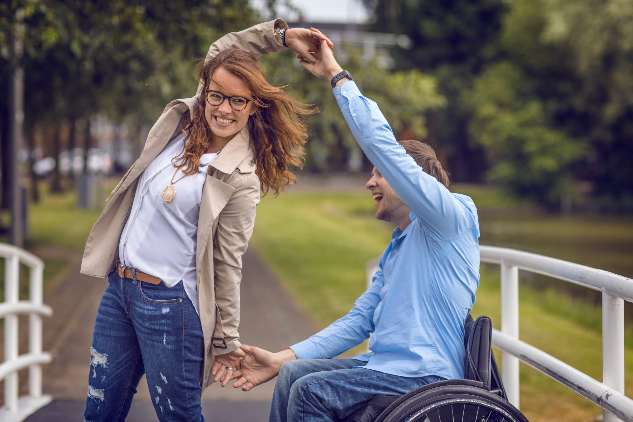 Wheelchair using young man and his girlfriend walking together through a city park on a sunny afternoon