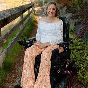 smiling woman in powerchair along side a wooden fence in a garden
