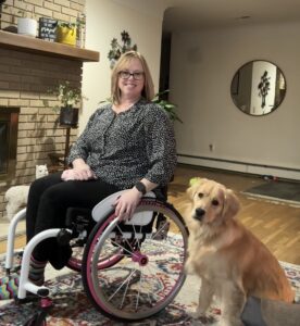 a woman in a wheelchair sits next to her service dog
