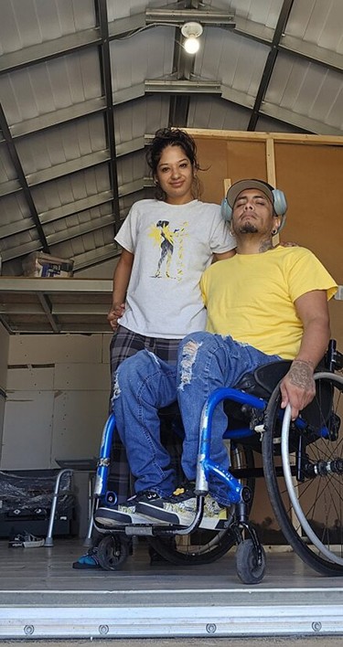 A woman stands next to a man in a wheelchair smiling