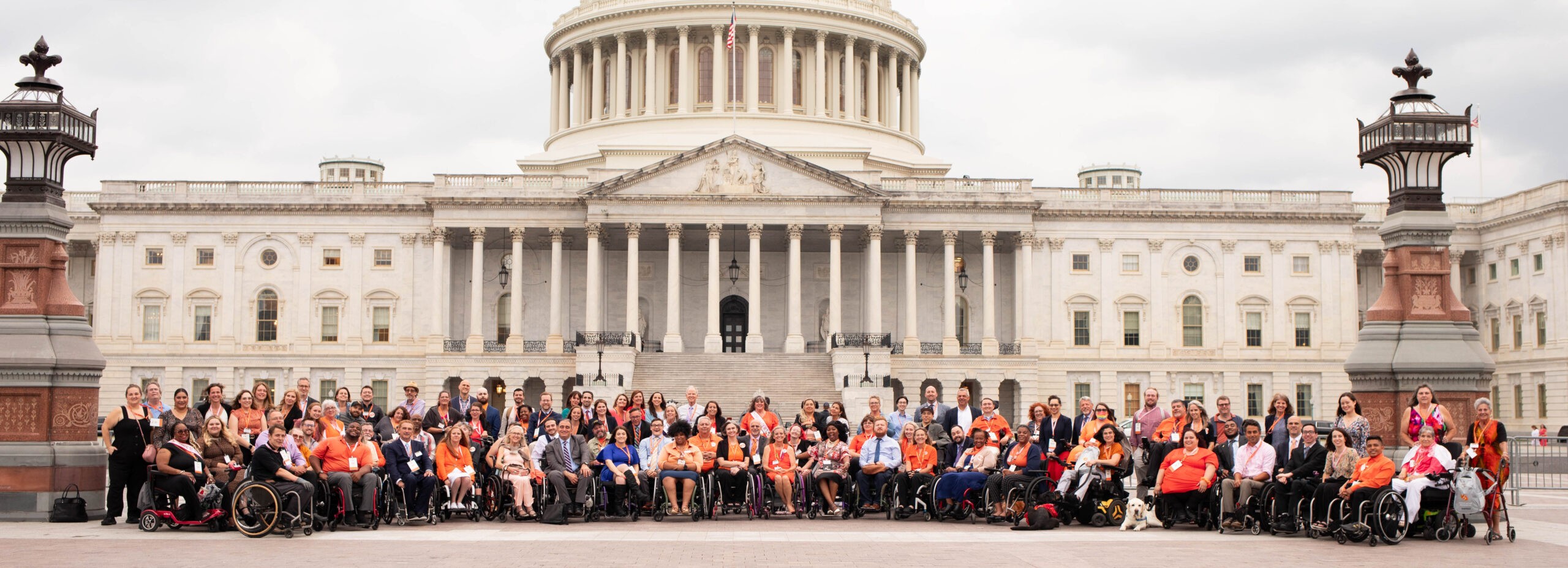 A large group of wheelchair users wearing orange sit in front of the US Capitol building.