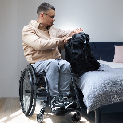 Young man opening his backpack while sitting in wheelchair 