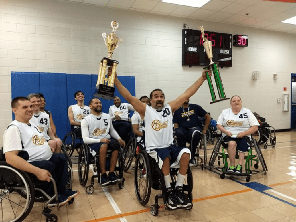 team of wheelchair basketball players ob tge court, one holding a trophy in each hand