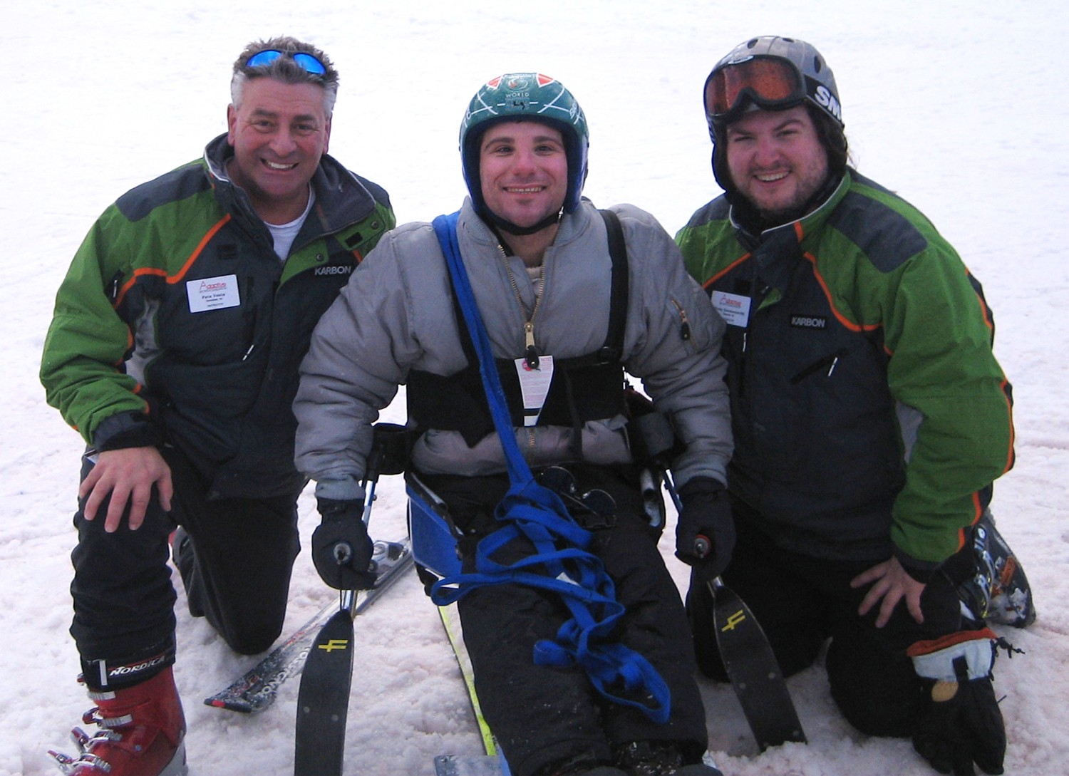 Man on on adaptive skis with a man on either side in the snow.