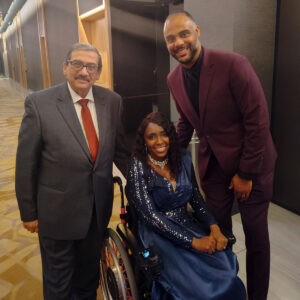 Woman in wheelchair with two men standing on either side, all smiling for camera