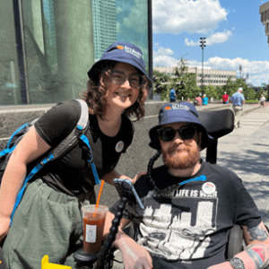 woman standing next to man in powerchair outside a building