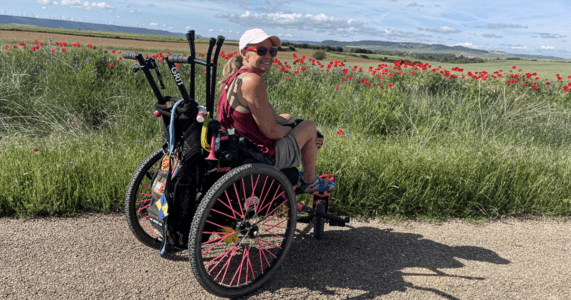 female wheelchair user on a trail in a field of red flowers with bright blue sky in the background