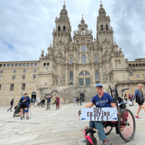 woman in wheelchair in front a cathedral holding a sign "Out enjoying life" 